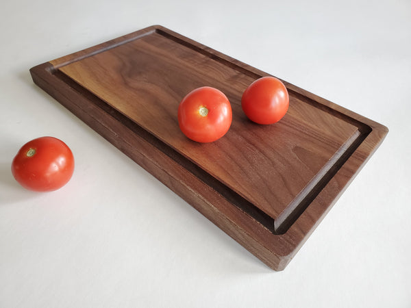Wooden cutting board with three tomatoes on a white background